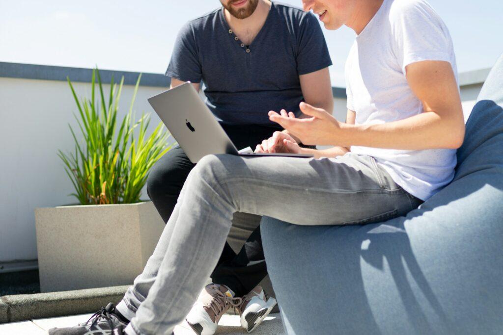 Zwei Mitarbeiter besprechen Datenschutzstrategien auf einem Balkon, einer mit einem Laptop, symbolisiert die Rolle eines externen Datenschutzbeauftragten in Karlsruhe bei der Unterstützung von Unternehmen in Datenschutzfragen.