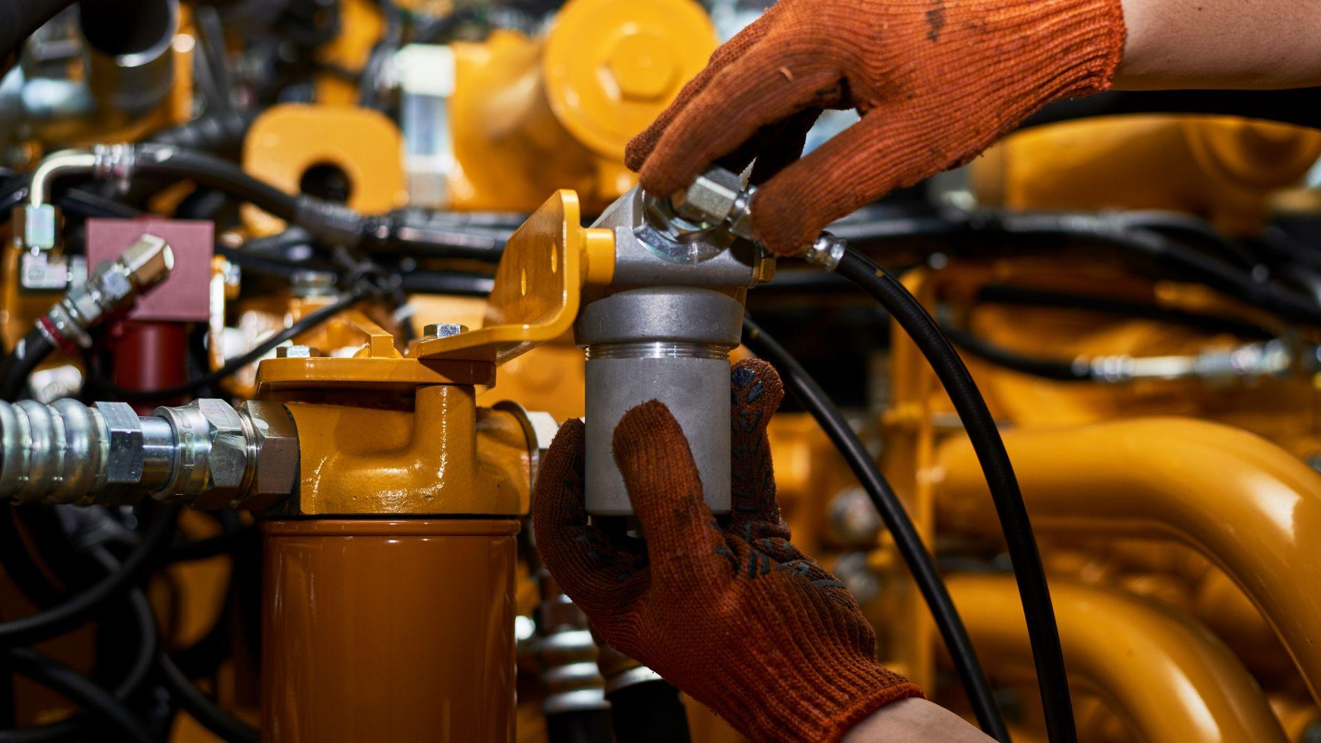 Mechaniker montiert hydraulische Verbindung an gelbem Aggregat mit Schnellkupplung und Schlauchanschluss