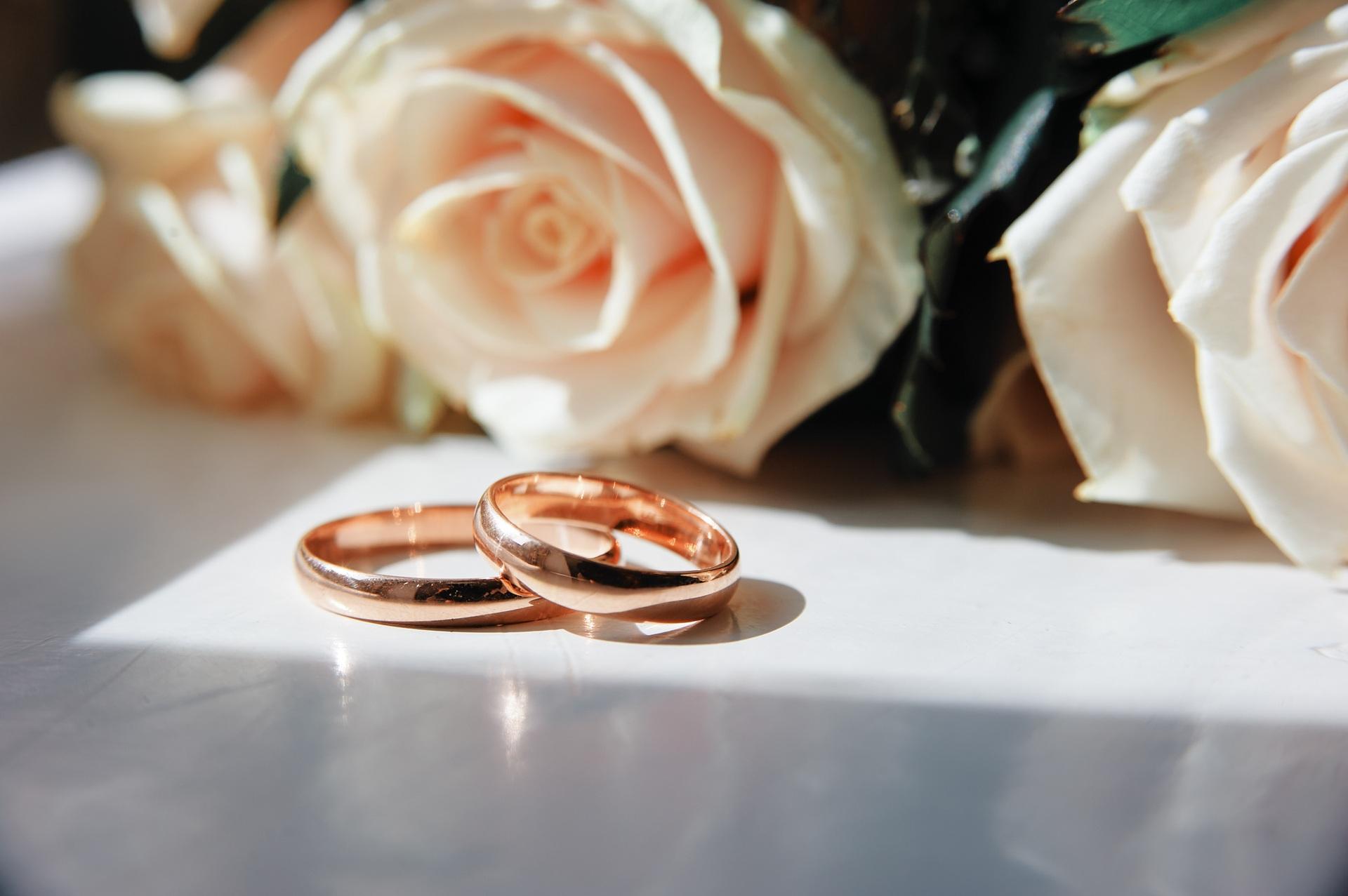 Roségold-Ringe mit Rosen im Hintergrund | Eheringe aus Gold

